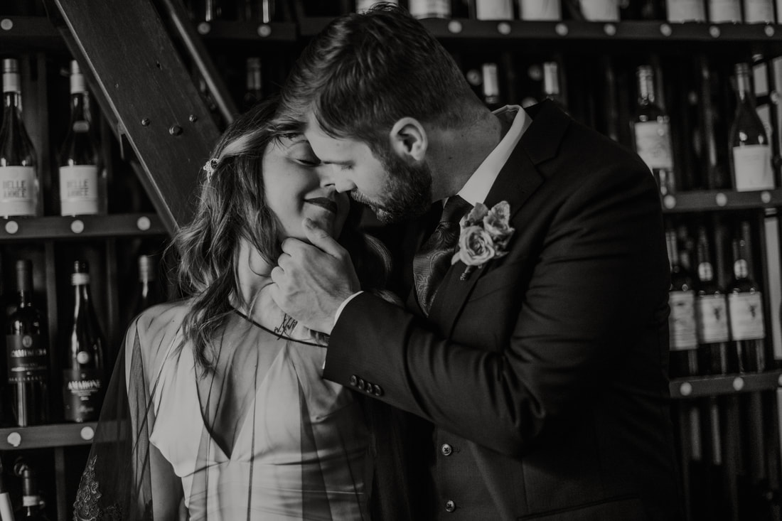 The Library Wine Bar and Bistro, Wallingford, CT: Black and white image of a husband leaning down to kiss his wife in front of a bookcase of wine bottles