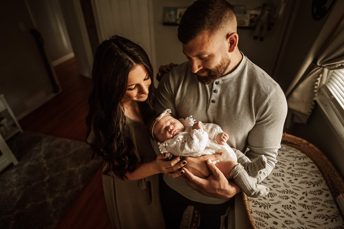 Stratford, Connecticut: A new father and mother gaze down smiling at their newborn daughter as sunshine streams through their nursery window